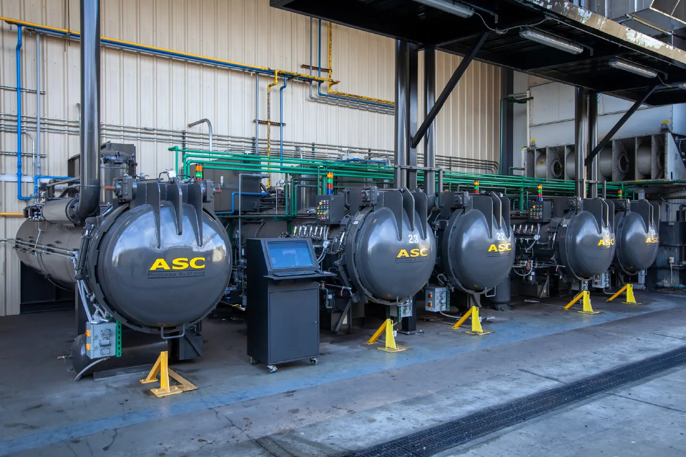 A row of ASC autoclaves installed side by side in a customer plant, with a shared operator station