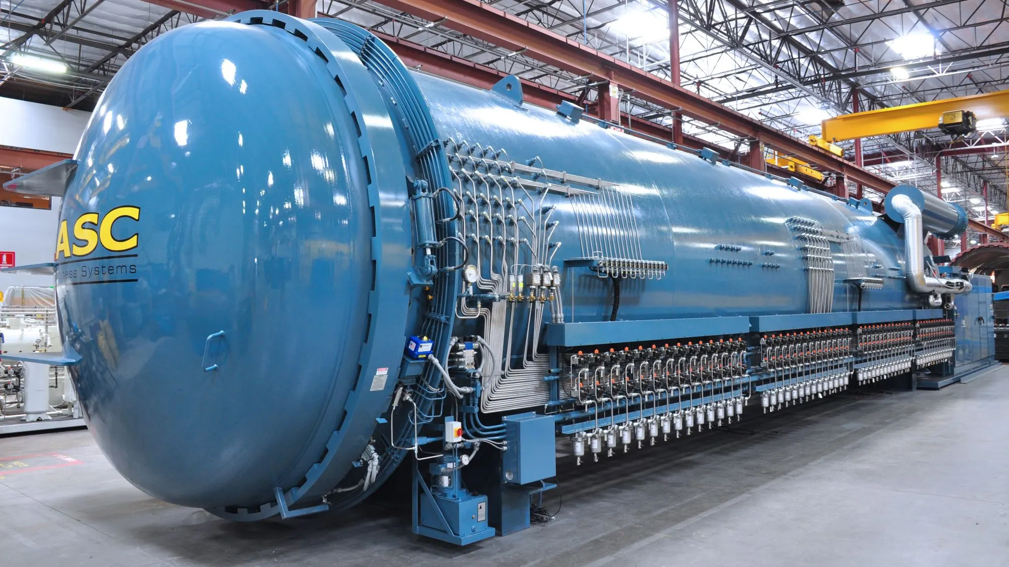 A long blue ASC Econoclave composite autoclave on the Valencia shop floor, its vacuum ports lining the vessel