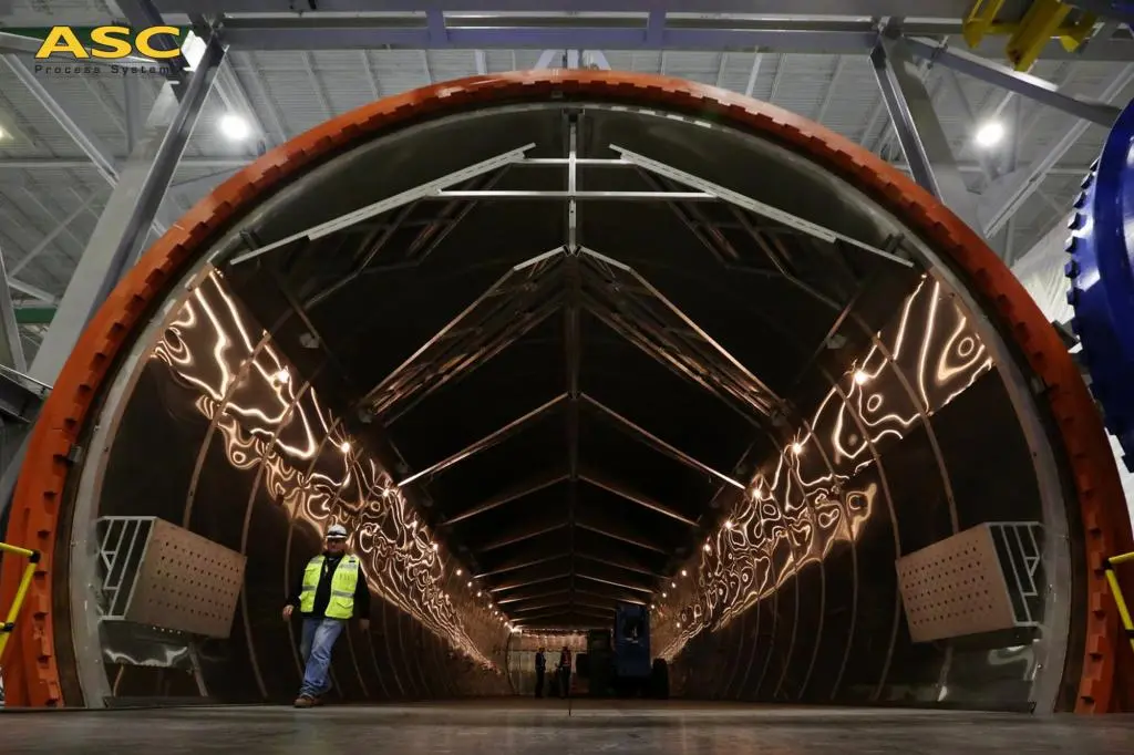 A worker inside the open door of a 28 ft × 120 ft ASC field-built autoclave