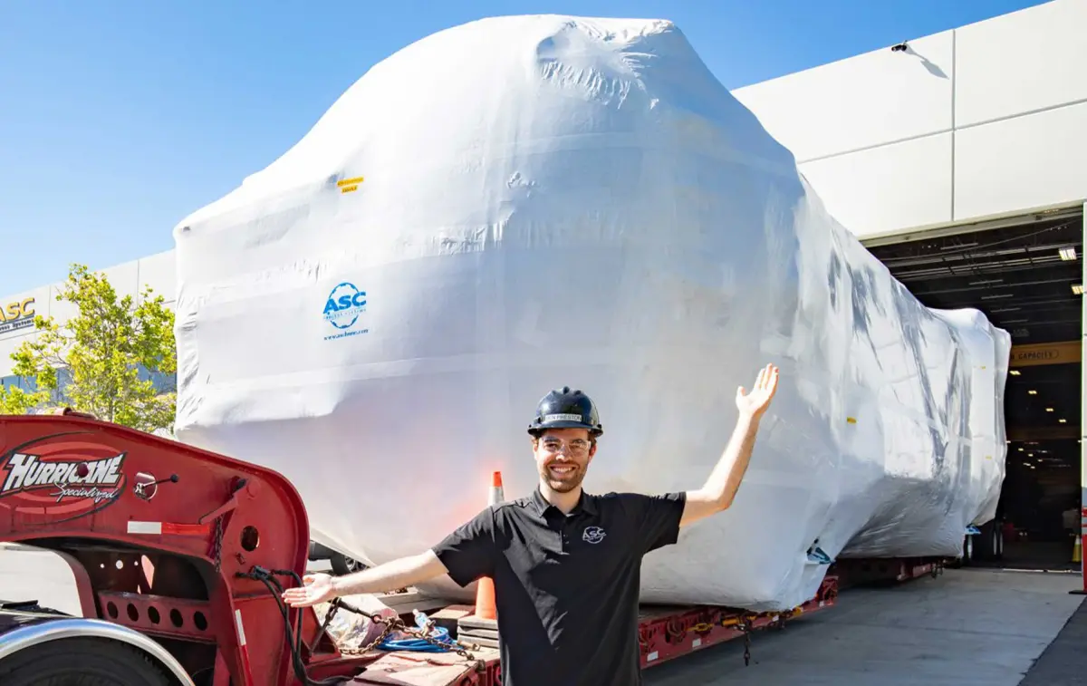 An ASC engineer in a hard hat presenting a shrink-wrapped autoclave loaded on its truck