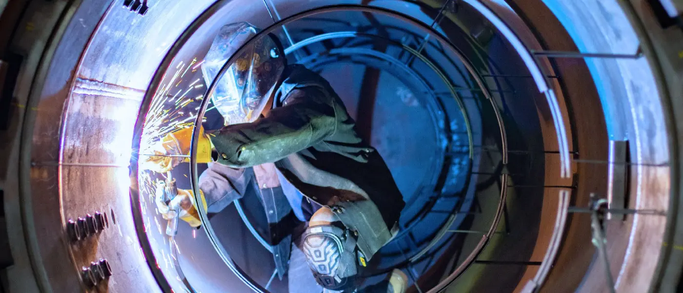 An ASC welder grinding inside a pressure vessel shell in a shower of sparks