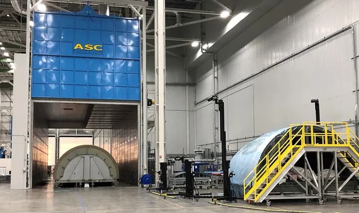 A tall ASC oven with its door raised and a large aerospace structure on a cart inside