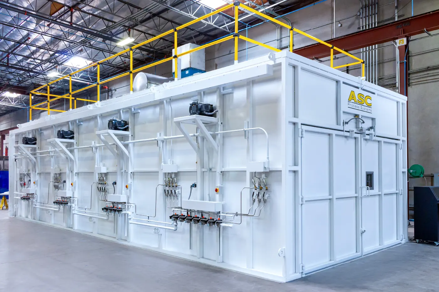 A large white ASC composite curing oven with its blowers and a guarded roof platform